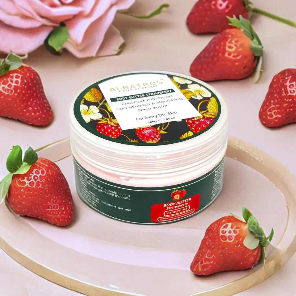 Jar of strawberry-flavored body butter surrounded by strawberries on a light surface.