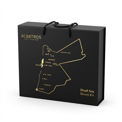 A black Albatros gift box with gold lettering and a gold outline map of the Dead Sea region, shown on a clean white background. The box includes black rope handles and is labeled 'ALBATROS A GIFT OF NATURE' and 'Dead Sea Beauty Kit'.